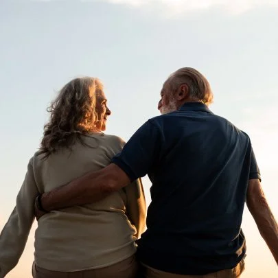 Casal idoso de costas, caminhando juntos ao pôr do sol.
