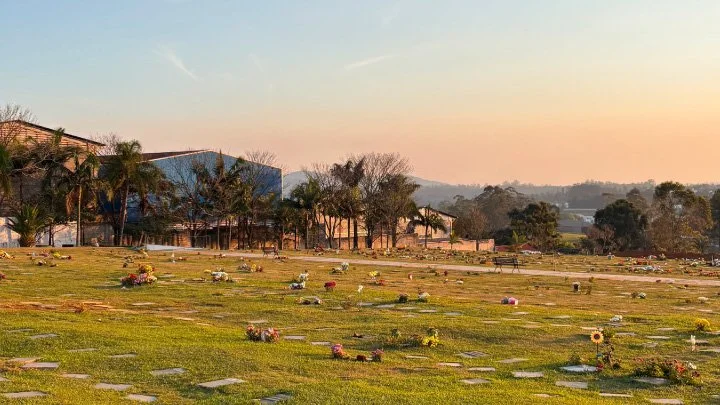 Cemitério com túmulos decorados com flores ao pôr do sol.