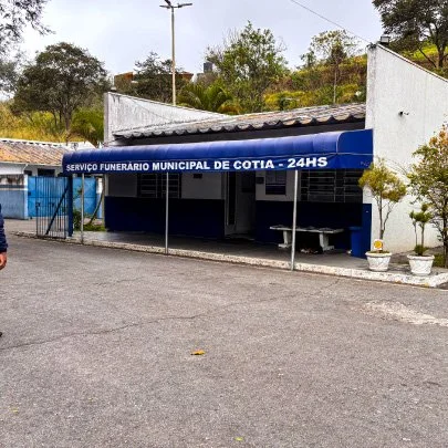 Fachada de um prédio do serviço funerário municipal de Cotia com um painel azul e uma bancada na frente.