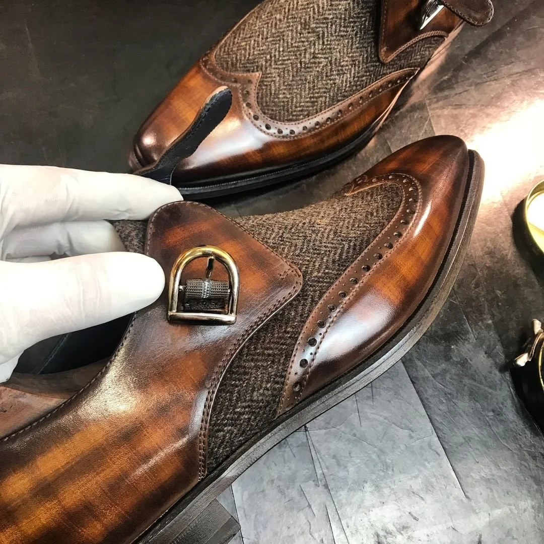 A pair of polished brown leather dress shoes with herringbone fabric accents and decorative brogue perforations.