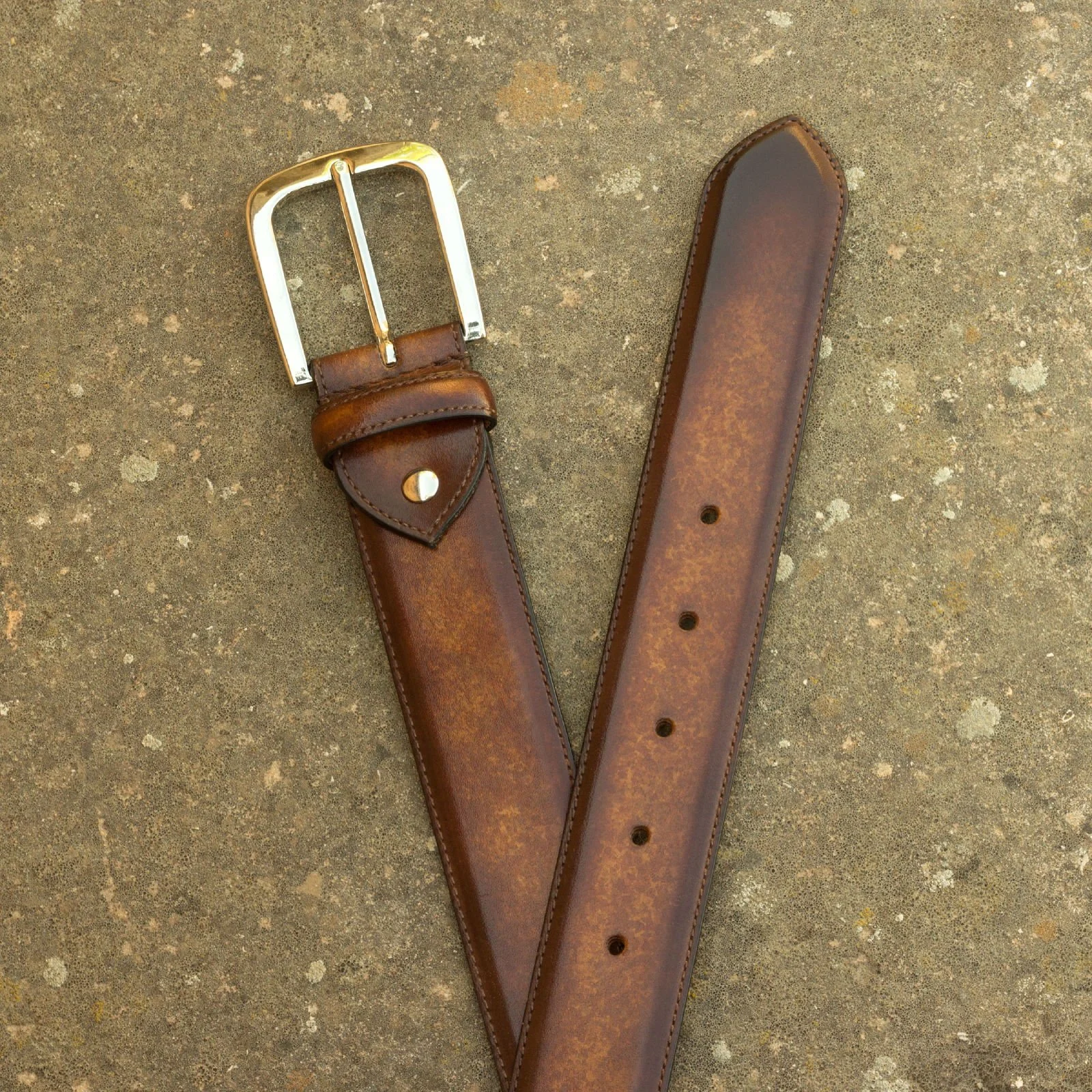 A brown leather belt with a silver buckle on a textured, neutral-colored background.