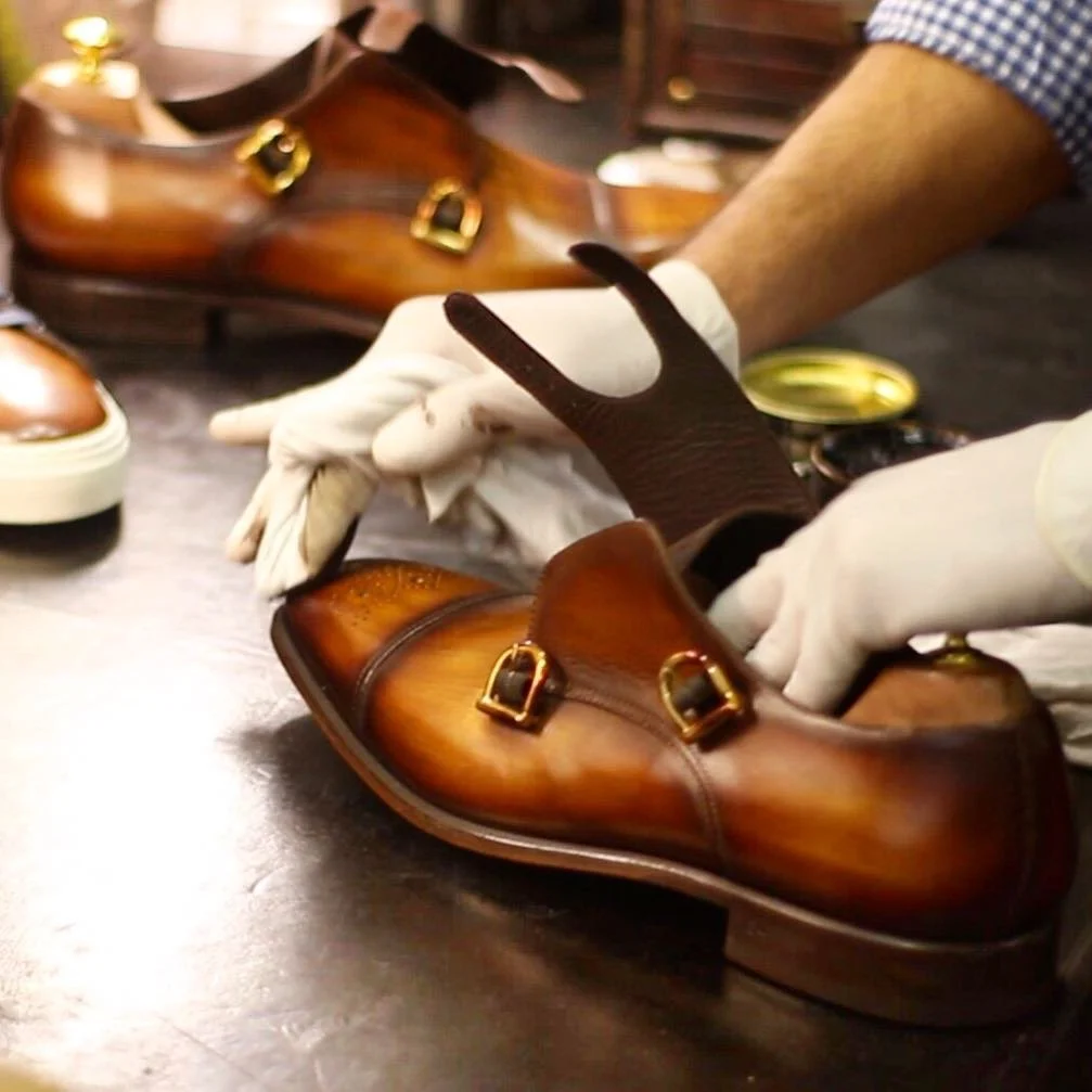 Person cleaning a pair of polished brown leather dress shoes with white gloves.