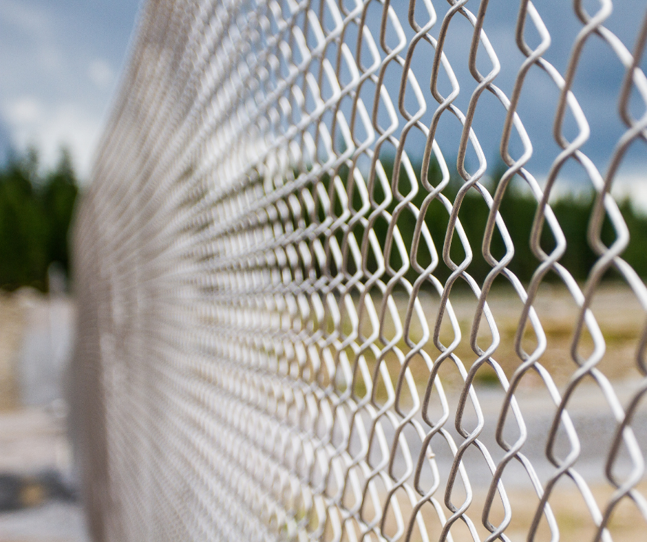 Close-up of a chain-link fence with blurred background of green trees and cloudy sky
