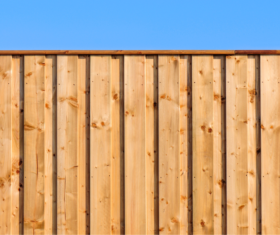 Close-up of a wooden privacy fence with vertical planks under a clear blue sky.