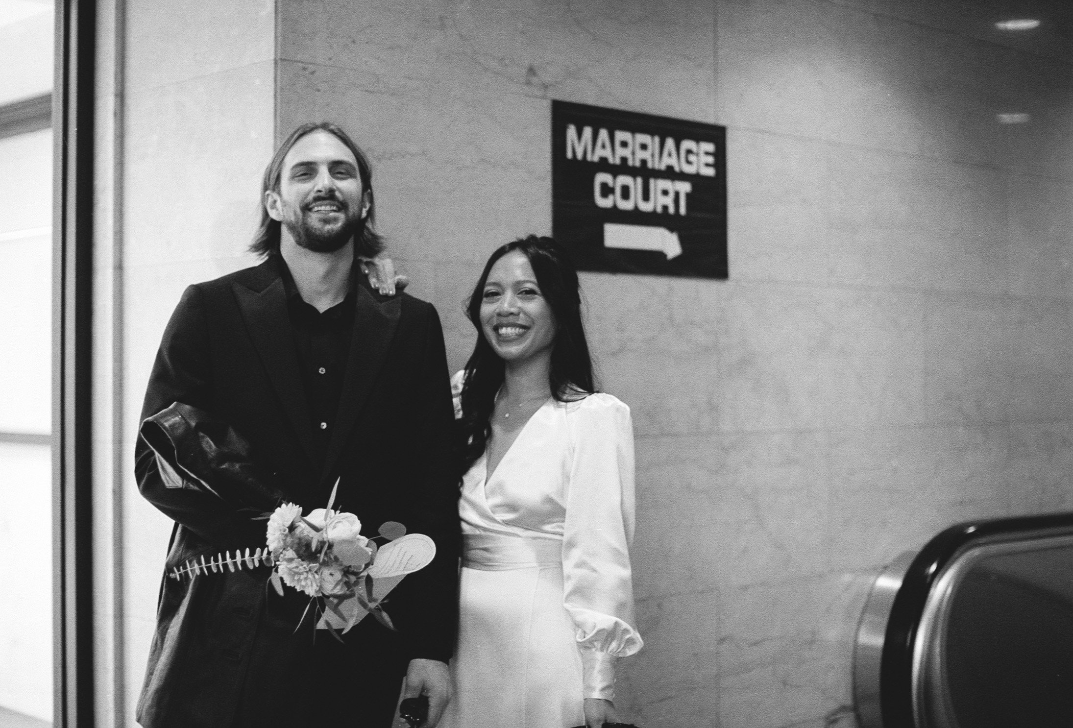 Bride and groom stand in front of marriage court sign at City Hall Elopement in downtown chicago to get married on film. Grace Coudal is a Chicago lesbian photographer specializing in portraits, candid, editorial, documentary, events, + weddings. An