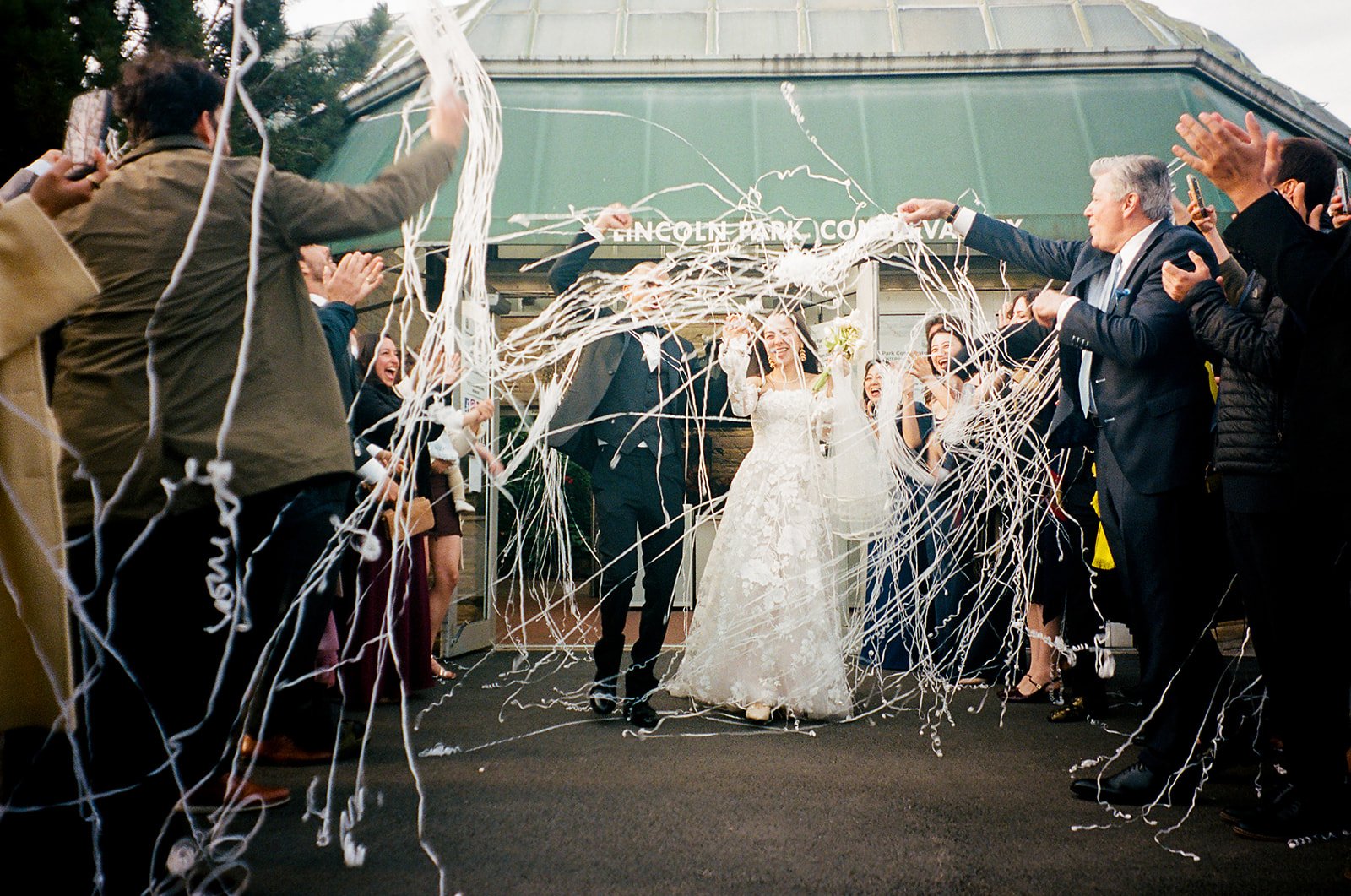 bride and groom exit ceremony and are covered in streamers. Bride and Groom get married at Lincoln Park Conservatory and Salvatores. Grace Coudal is a Chicago lesbian photographer specializing in portraits, candid, editorial, documentary, events, + w