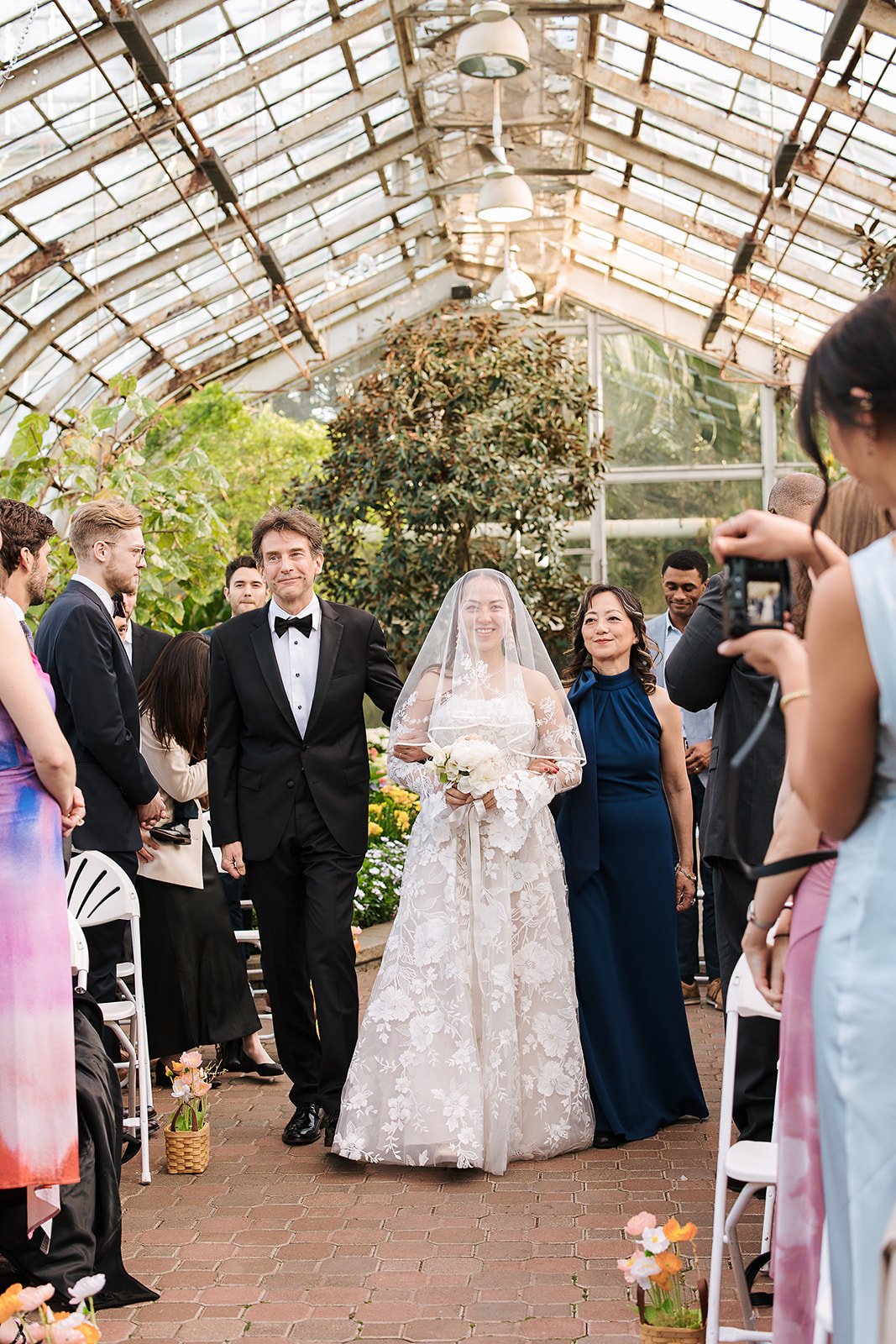 bride walks down natural lit aisle. Bride and Groom get married at Lincoln Park Conservatory and Salvatores. Grace Coudal is a Chicago lesbian photographer specializing in portraits, candid, editorial, documentary, events, + weddings. Analog film wed