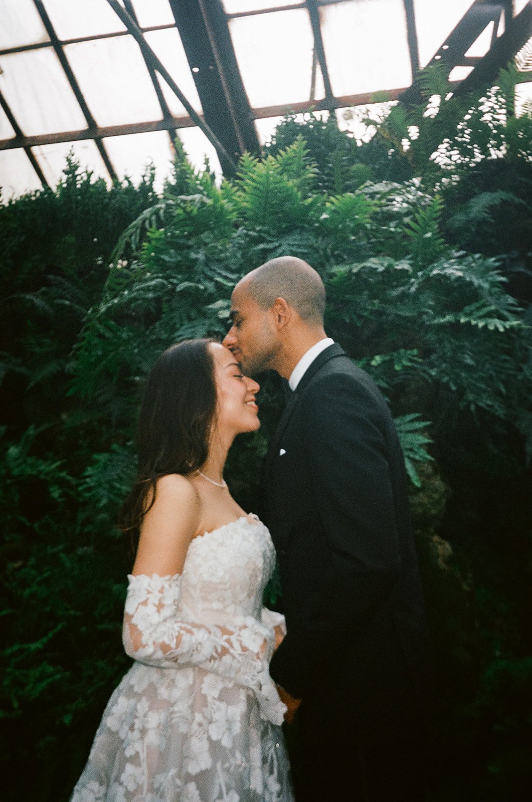groom kisses brides forehead around lush plants. Bride and Groom get married at Lincoln Park Conservatory and Salvatores. Grace Coudal is a Chicago lesbian photographer specializing in portraits, candid, editorial, documentary, events, + weddings. An