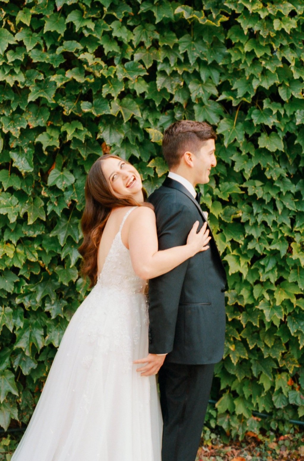 bride and groom hug and laugh in front of ivy wall. Luxury, high-end wedding photographer shot on film. Grace Coudal is a Chicago lesbian photographer specializing in portraits, candid, editorial, documentary, events, + weddings. Analog film wedding