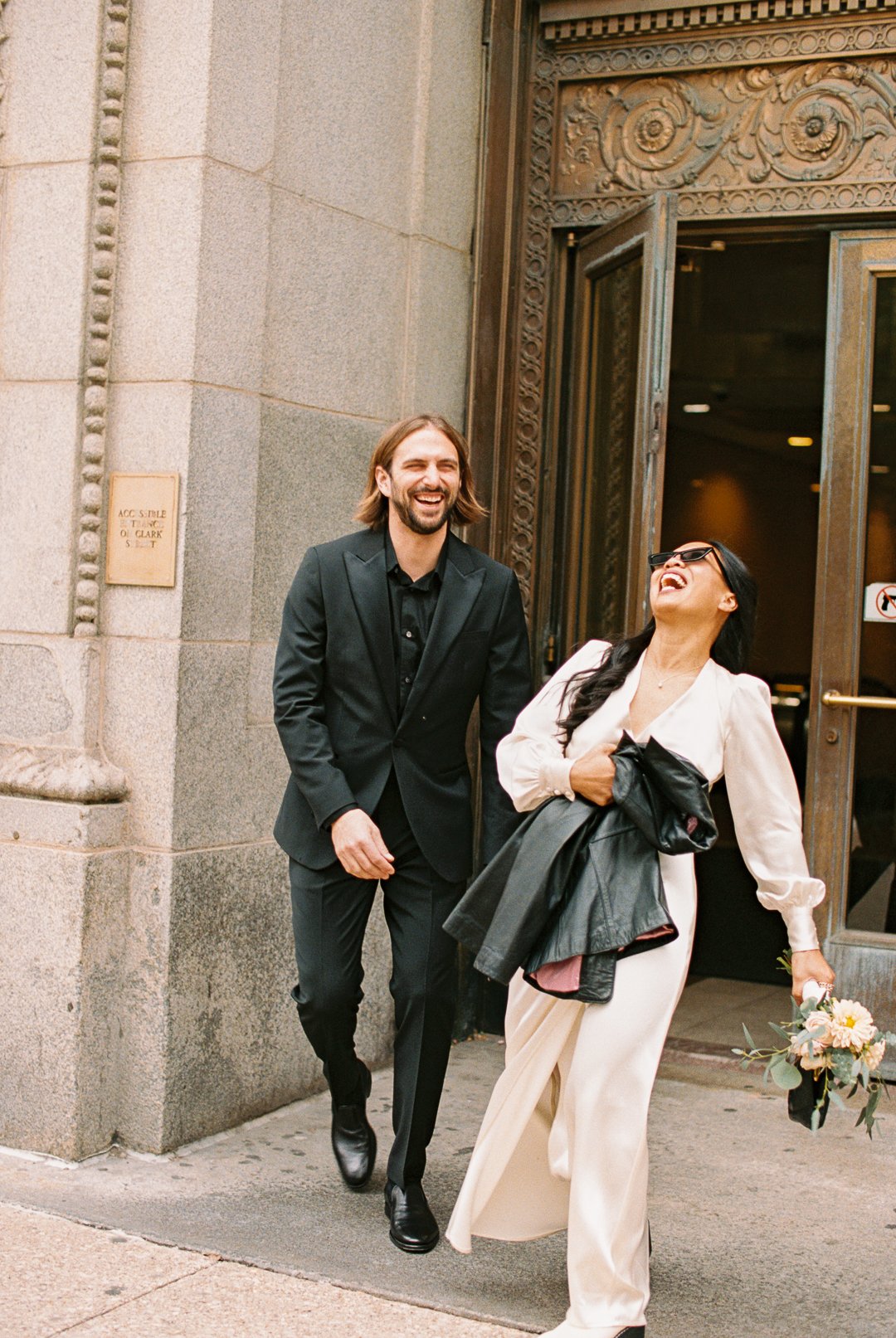 Bride and groom laugh leaving City Hall Elopement in downtown chicago. Grace Coudal is a Chicago lesbian photographer specializing in portraits, candid, editorial, documentary, events, + weddings. Analog film wedding photography, queer-owned.