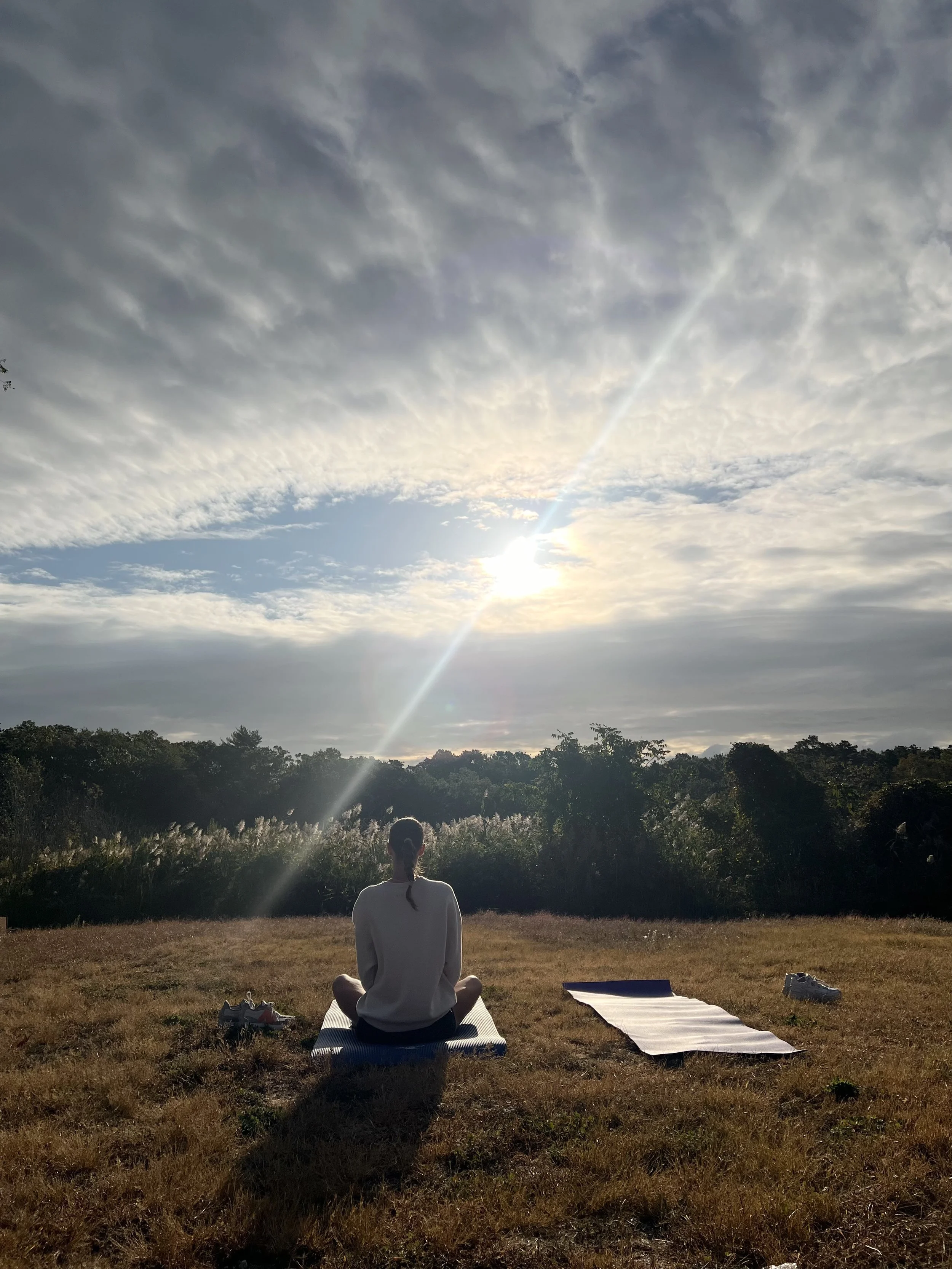 Persona haciendo yoga en un campo con vista al cielo soleado y nublado.