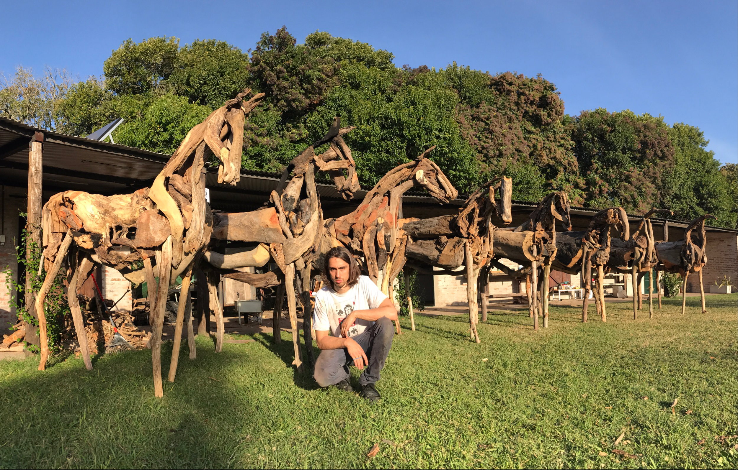 Estatua de caballos hechos con madera en un área al aire libre con un hombre agachado frente a ellos.
