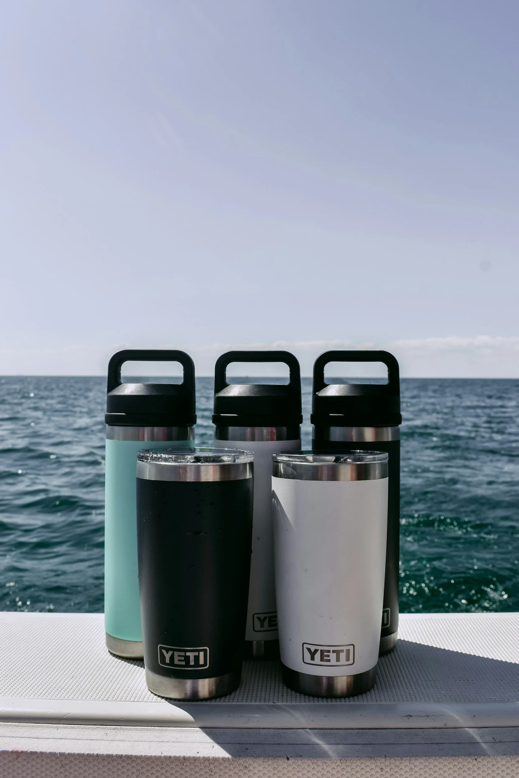 Six YETI brand insulated bottles on a boat with ocean in background.