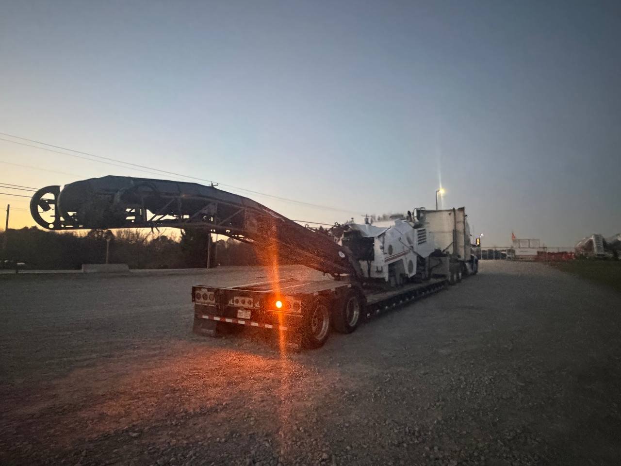 A large truck with a flatbed trailer transporting a dismantled spacecraft or rocket at dusk or dawn.
