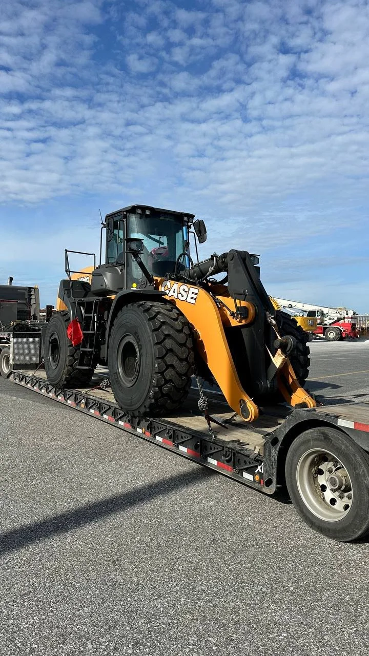 A CASE front loader construction vehicle loaded onto a flatbed truck, parked outdoors under a partly cloudy sky.