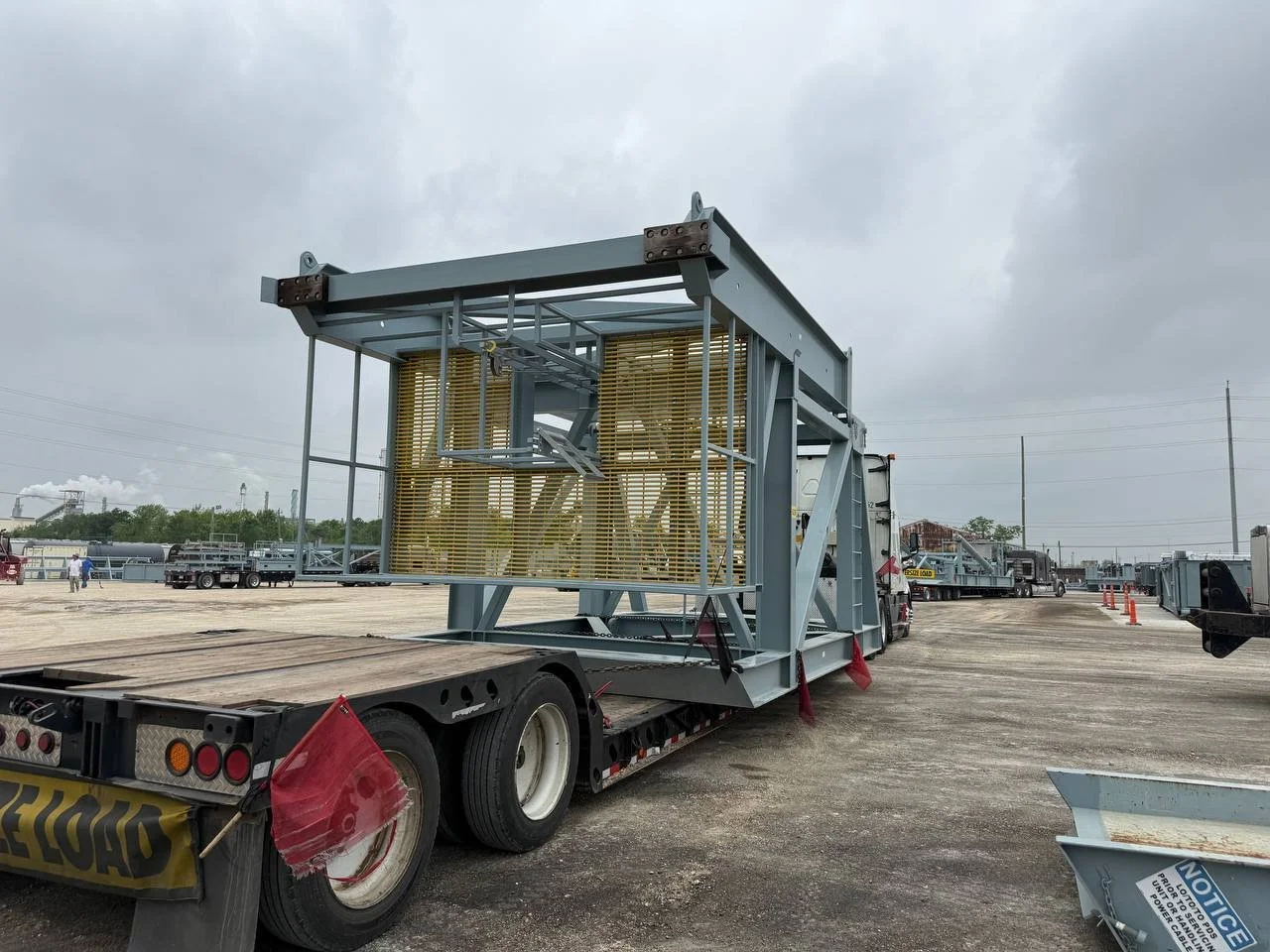 Large industrial structure loaded on a flatbed truck at an outdoor lot, with overcast sky and other trucks in the background.