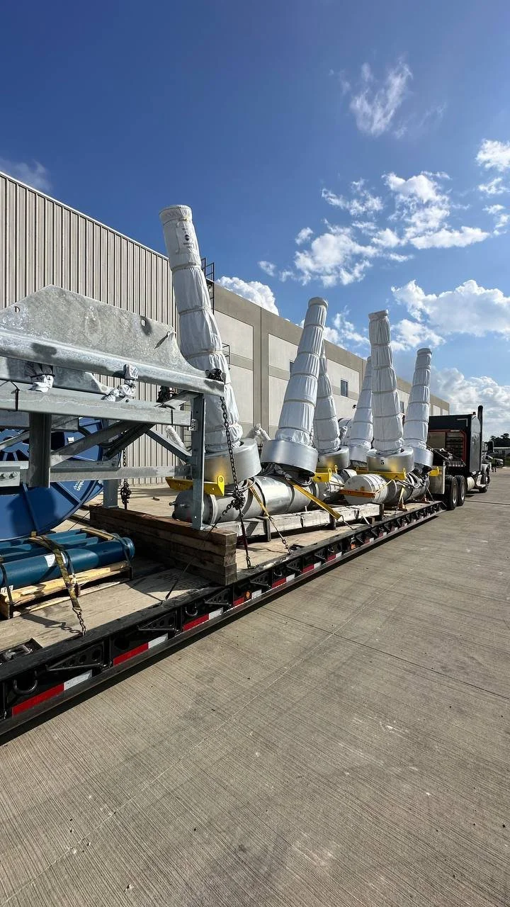 Large industrial equipment with tall, white, cone-shaped structures on a flatbed truck parked outside a warehouse.
