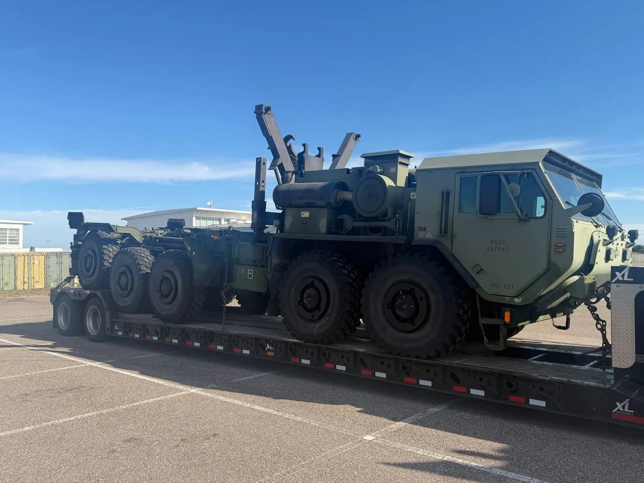 Military vehicle on a flatbed trailer in a parking lot.