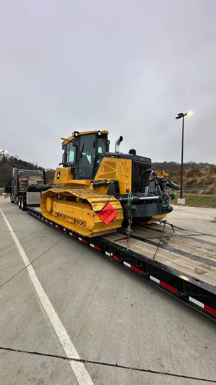 Yellow bulldozer loaded on a flatbed truck in an outdoor parking lot under cloudy sky.