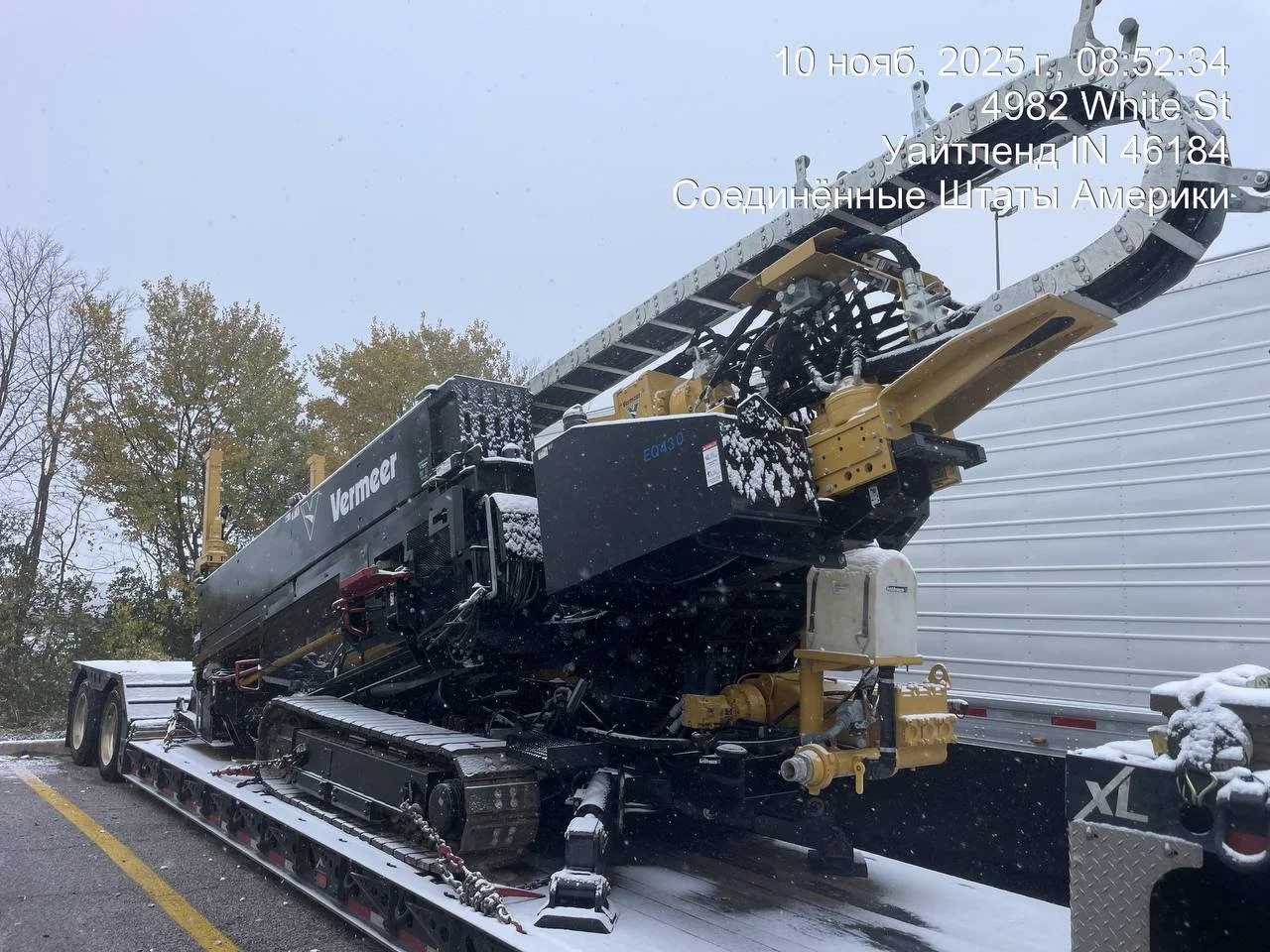 A large Vermeer drilling machine on a trailer, parked beside a white trailer, with snow on the ground and trees in the background.