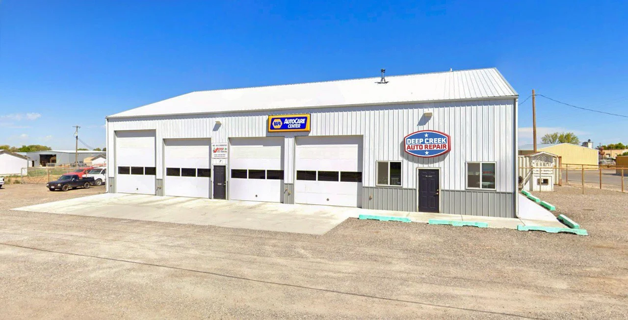 Auto repair shop building with four garage doors, signs for Deep Creek Auto Repair and NAPA AutoCare Center, and a black door.