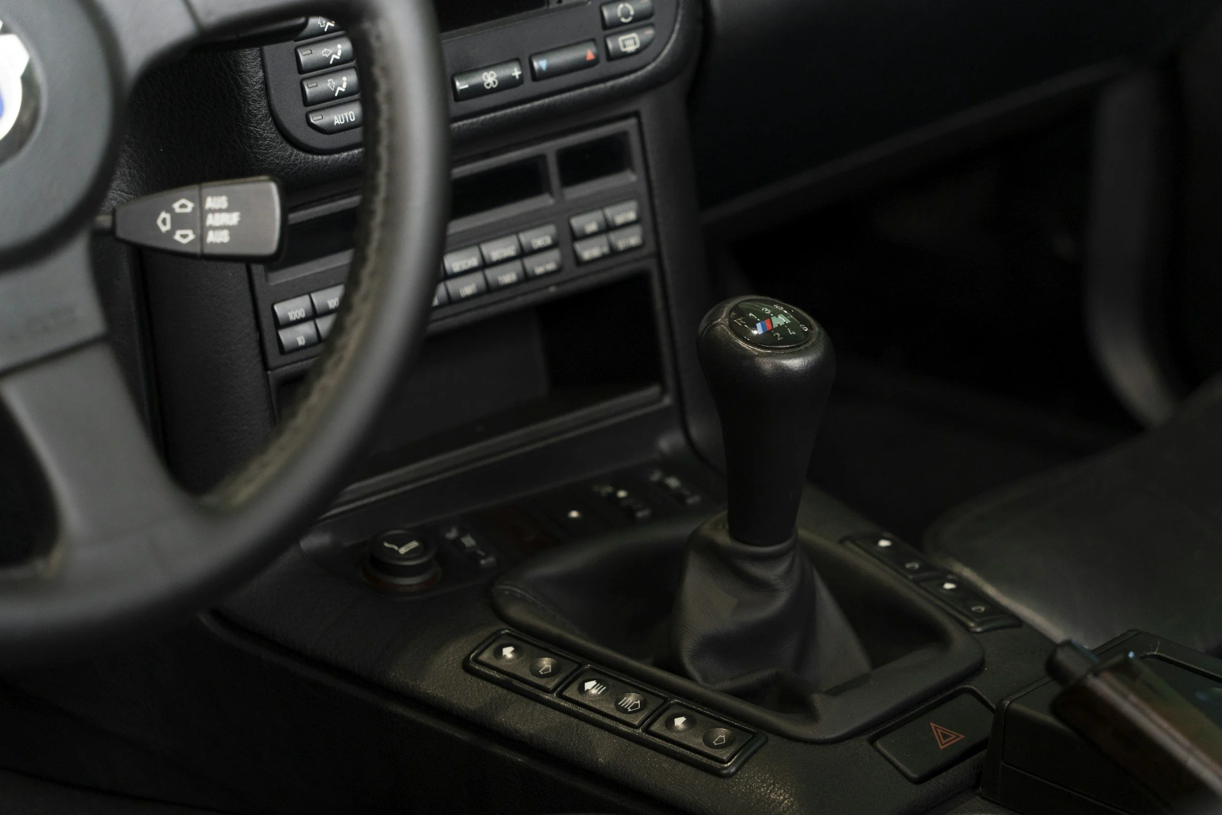 Close-up of a car's interior dashboard showing various buttons, a gear shift with a leather cover, and part of the steering wheel.