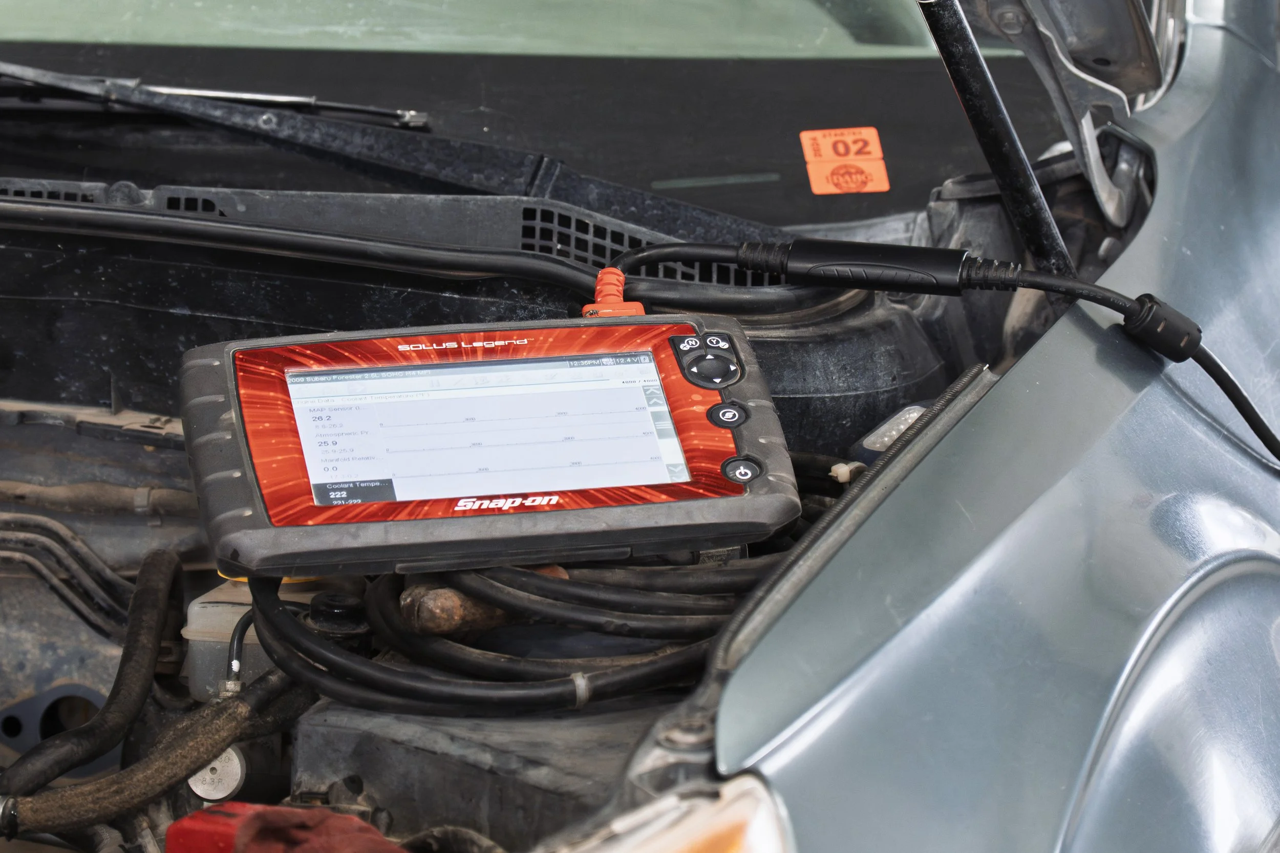 A diagnostic scan tool connected to a vehicle's engine with a display screen showing data, placed within the engine bay.