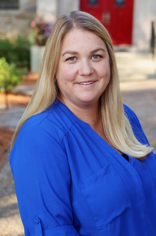 A woman with long blonde hair, wearing a blue shirt, outdoors with blurred background.