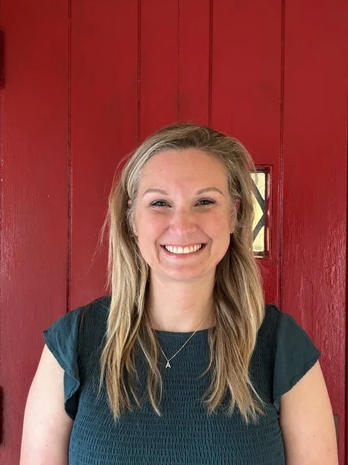 A smiling woman with long blonde hair in front of a red wooden background.