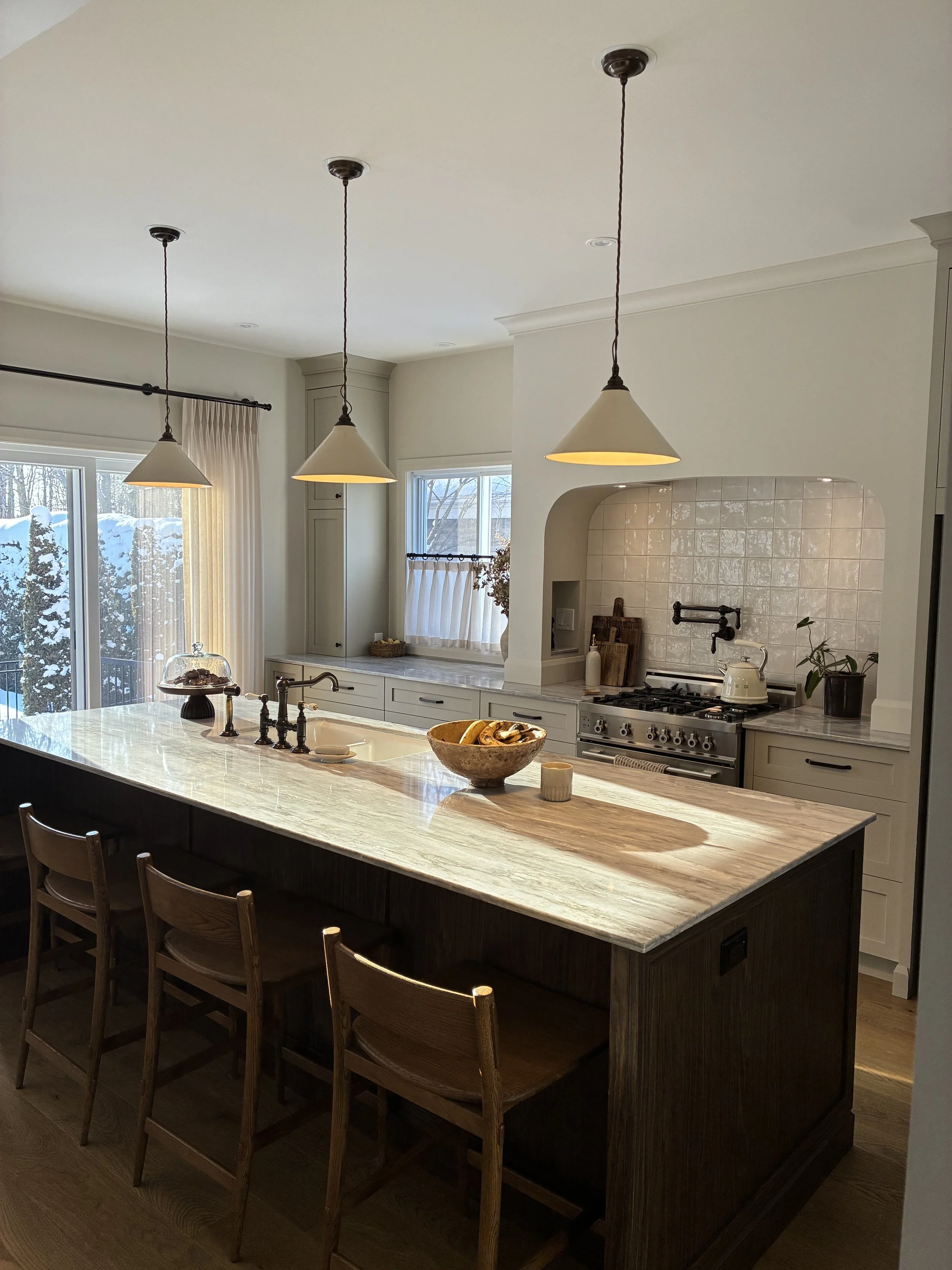 Cuisine moderne avec îlot en marbre, éclairage suspendu, fenêtres avec vue sur la neige, plan de travail, et appareils en acier inoxydable.