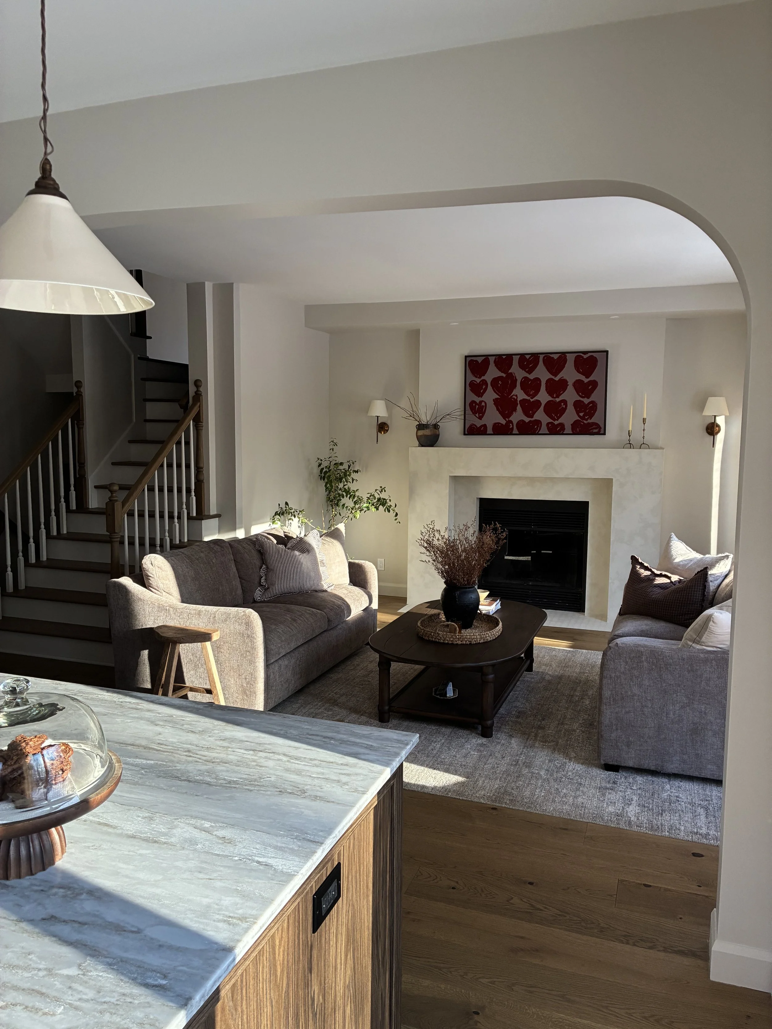 Salon moderne avec canapé gris, cheminée, œuvres d'art rouge à cœur, table basse en bois, aurore et plantes décoratives.
