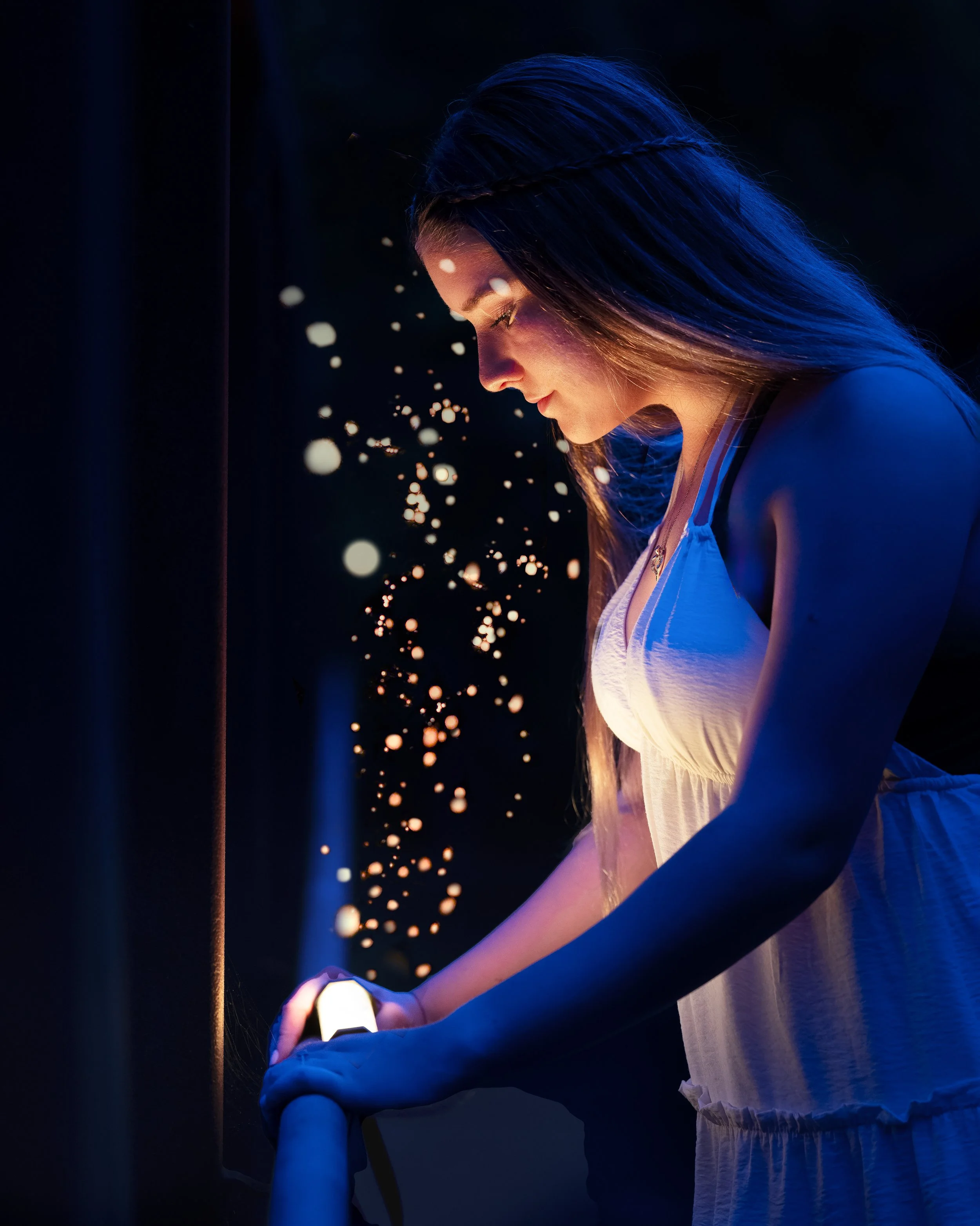 Young woman with long dark hair and light skin illuminated by blue and purple lighting, looking down at a smartphone in her hand, with an expression of focus and curiosity.