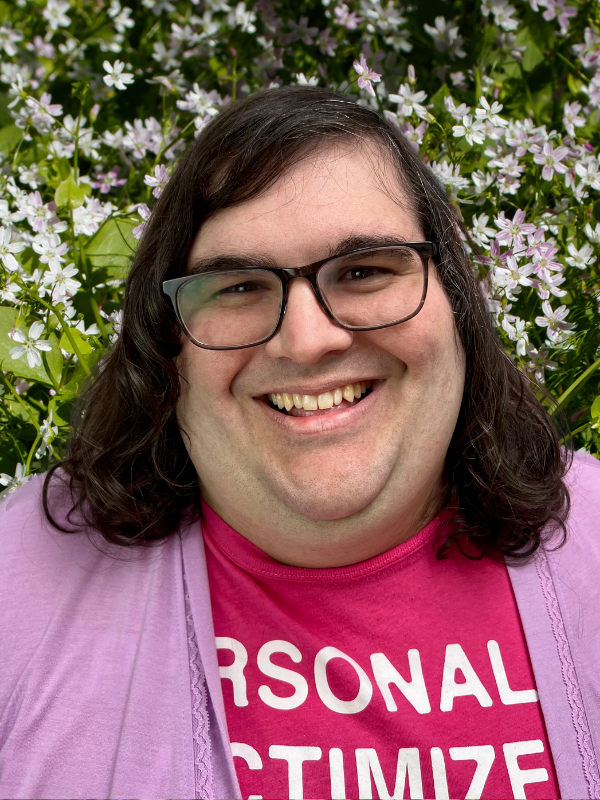 Headshot of Ellie smiling, she has shoulder length brown hair and wears glasses