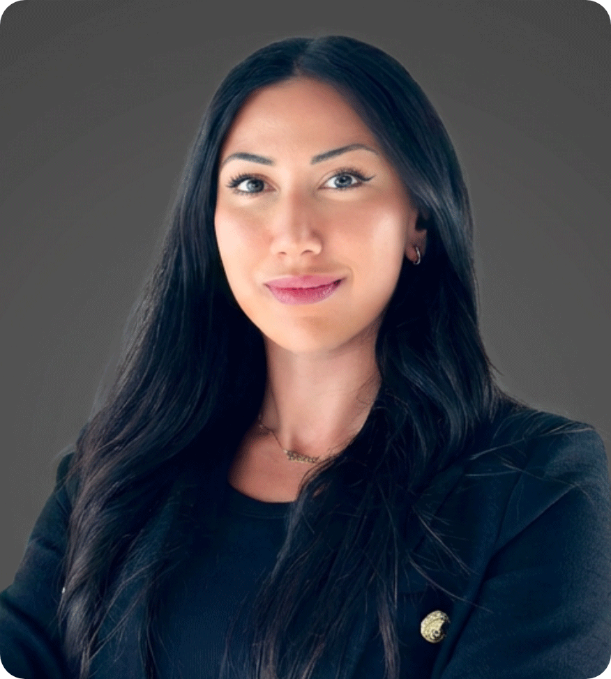 Professional woman with long black hair, wearing a dark blazer and jewelry, smiling at the camera against a neutral background.
