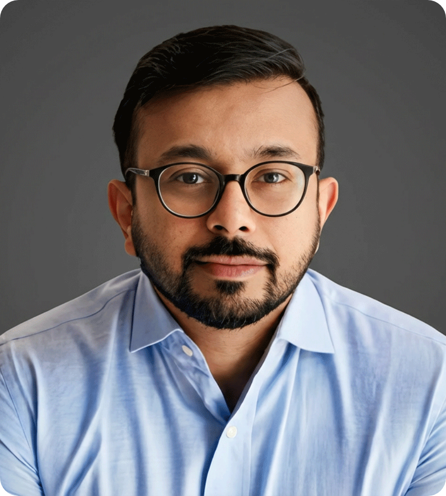 A man with dark hair and glasses wearing a light blue button-up shirt against a gray background.