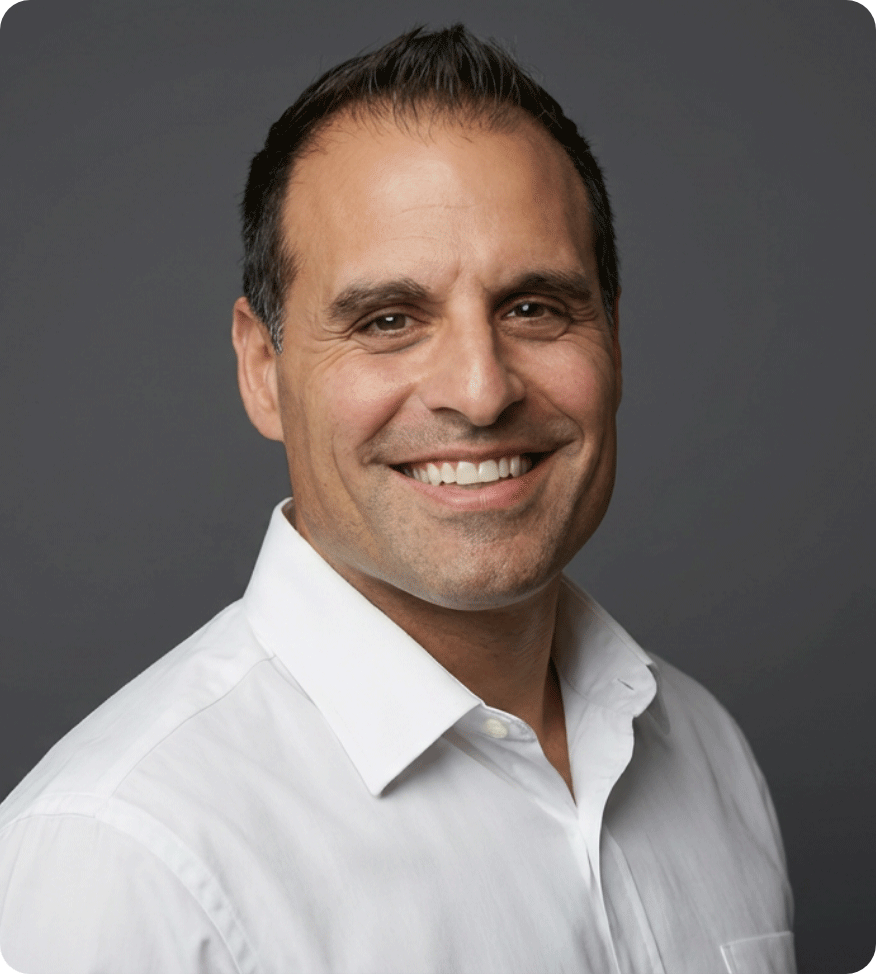 A smiling man with short dark hair wearing a white collared shirt against a gray background.