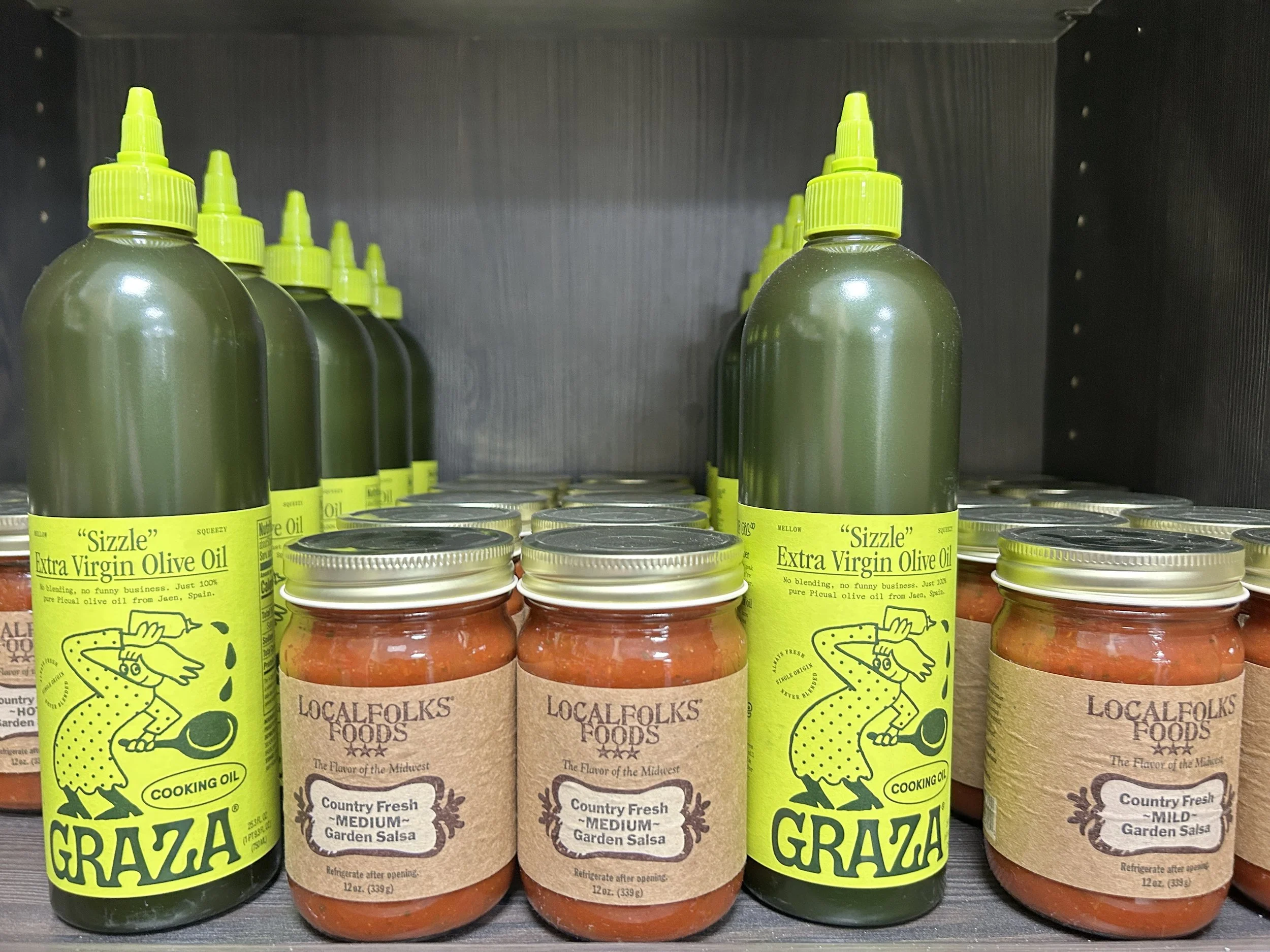 Shelves at Roots Market with bottles of Graza Extra Virgin Olive Oil and jars of Localfolks Foods garden salsa in a store
