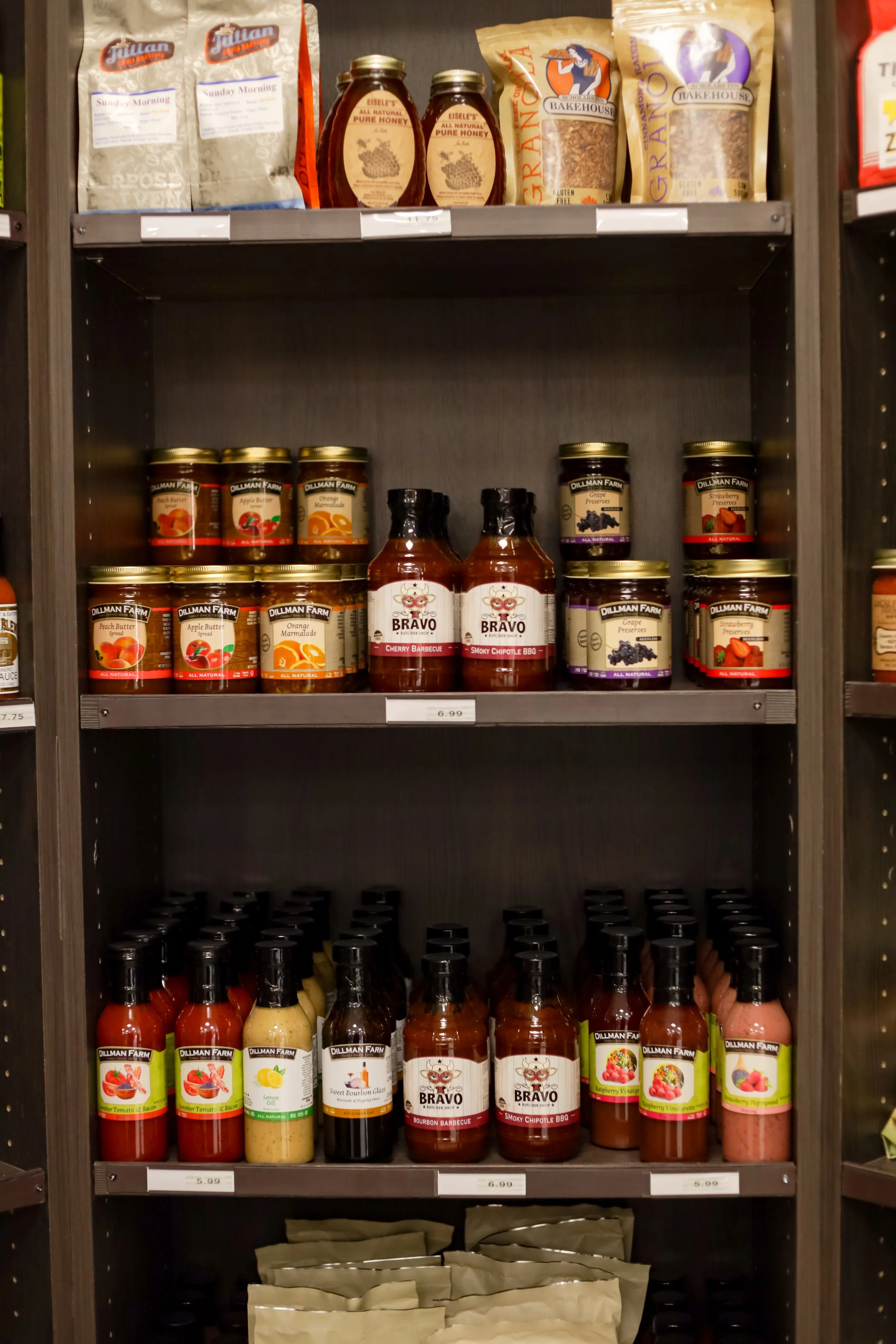 Shelf at Roots Market with jars of honey, jars of fruit preserves, bottles of BBQ sauce, and various bottled condiments.