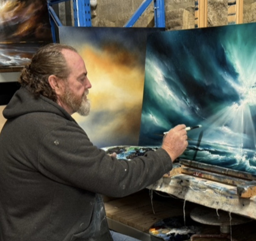A man painting a vibrant abstract nature scene on a large canvas, with an emphasis on blue and white hues, in an art studio.