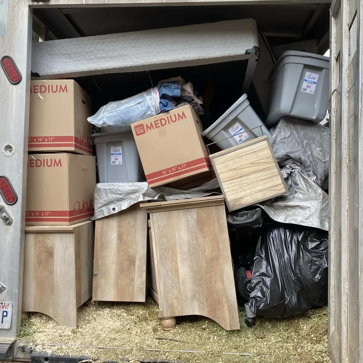 Packed moving truck containing cardboard boxes, plastic storage bins, wooden furniture, a mattress, and various household items.