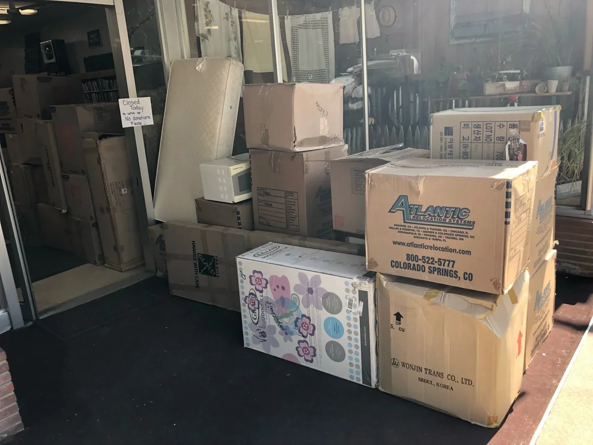 Stack of unpacked boxes and appliances outside a storefront with a sign that says "Closed Today" and "No donations Please"