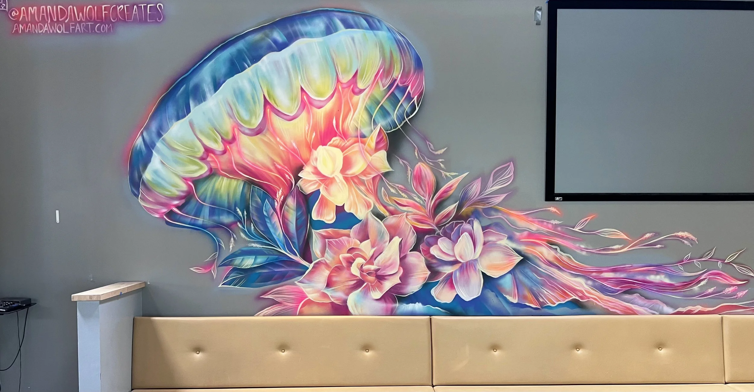 Colorful mural of a jellyfish with flowing tentacles and floral elements on a gray wall in a room with a beige bench and a mounted television.