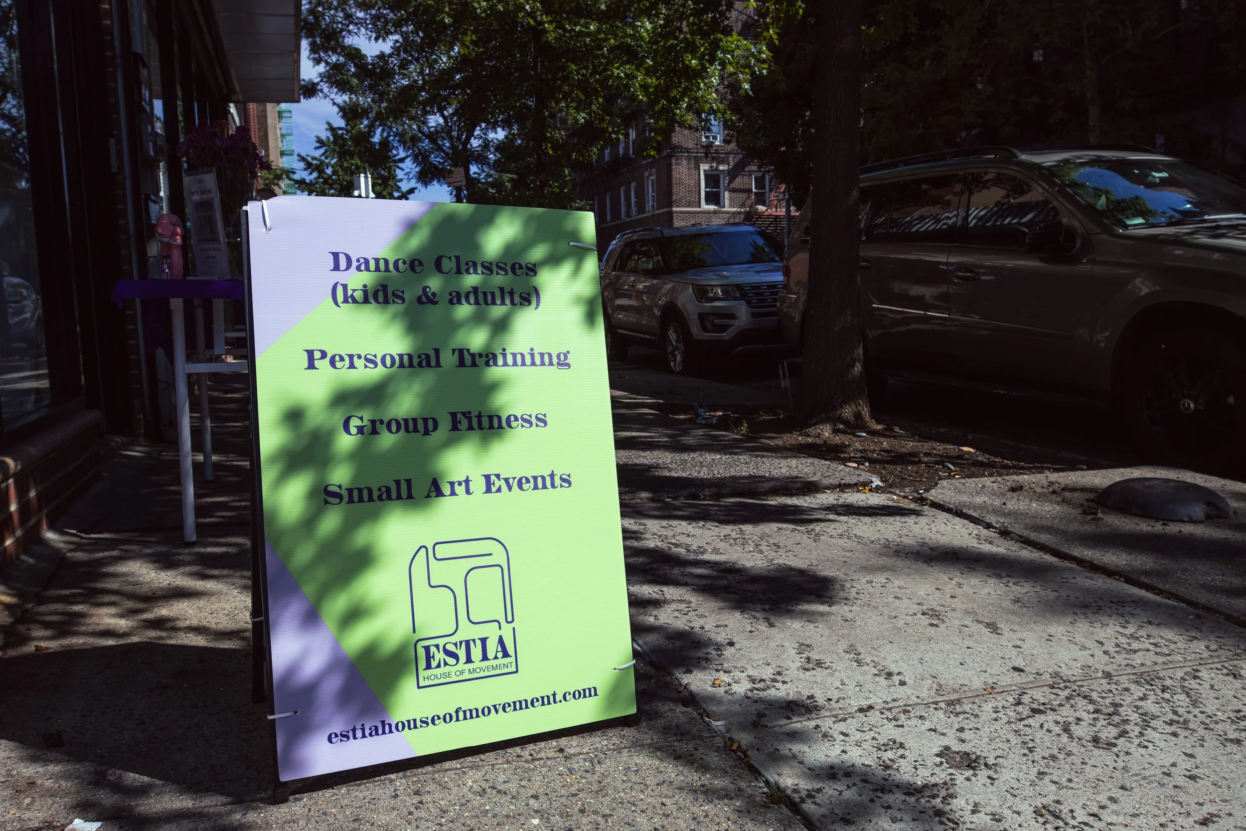 Sidewalk sign outside ESTIA House of Movement advertising dance classes, personal training, group fitness, and small art events.