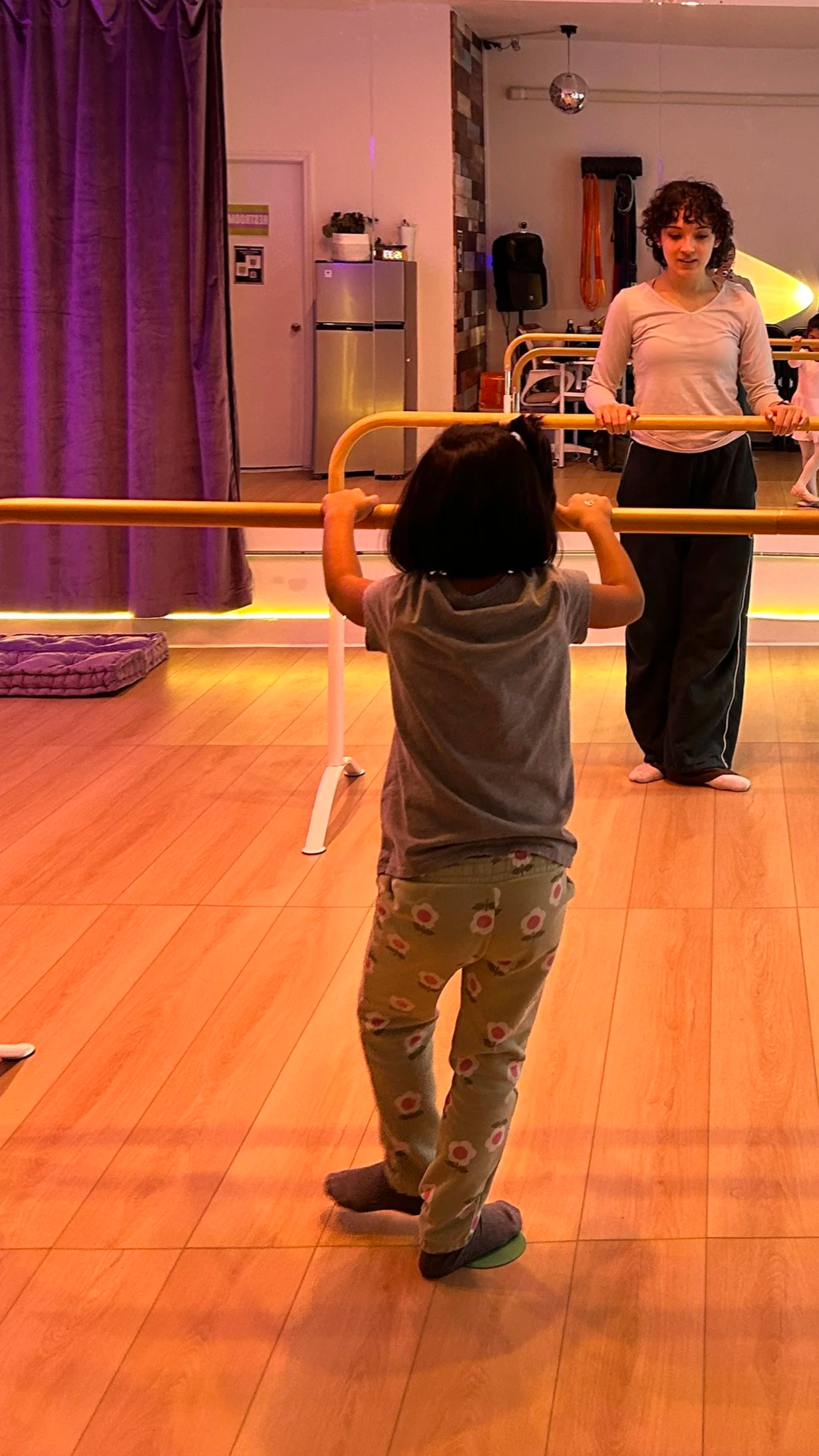 Dance instructor teaching a child basic ballet technique at the barre during a class at ESTIA House of Movement.