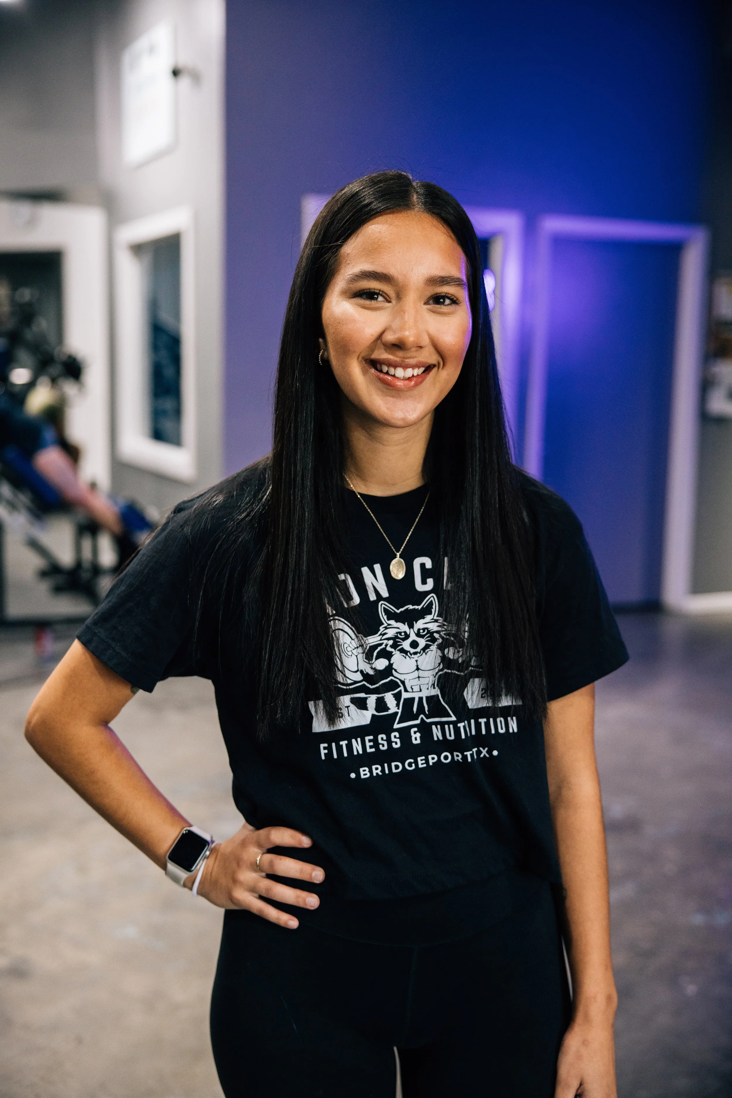 A woman smiling and posing with her hand on her hip in a gym.