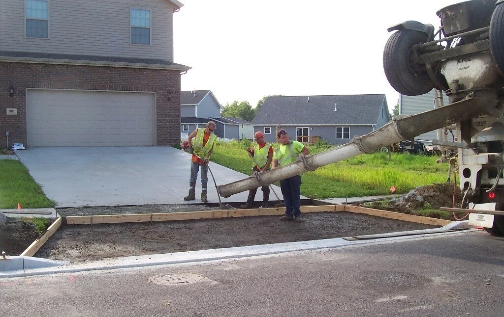 Construction workers pouring concrete into a new driveway with a concrete mixer truck.