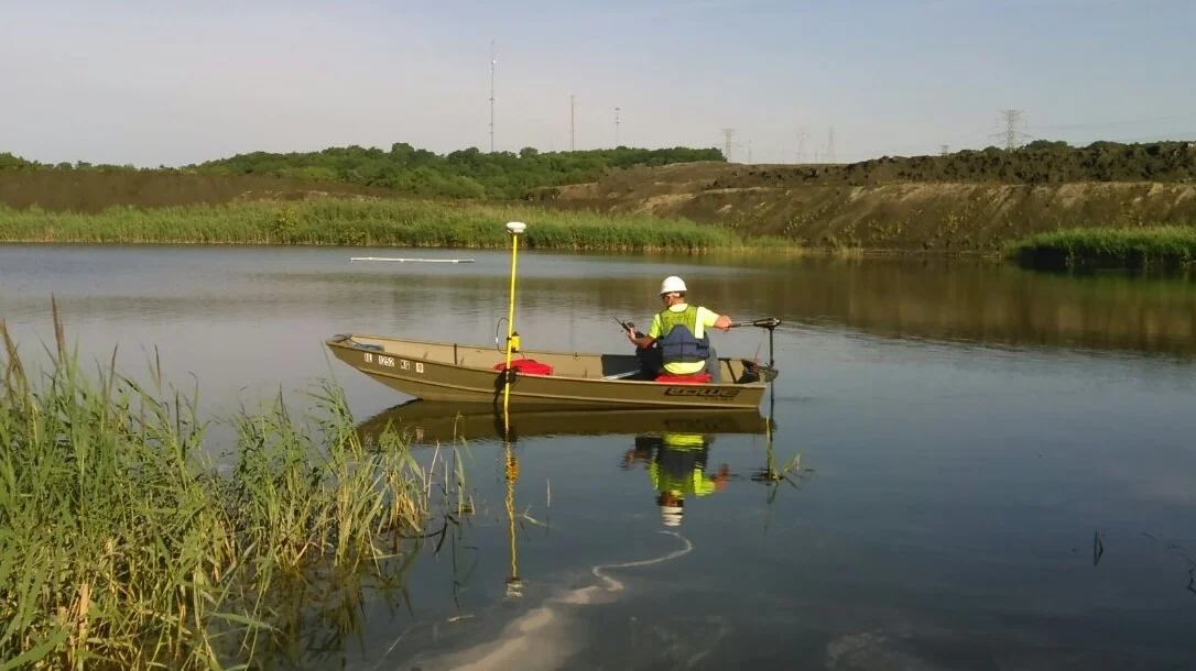 Person in a small boat on a calm river with grassy banks and distant hills.