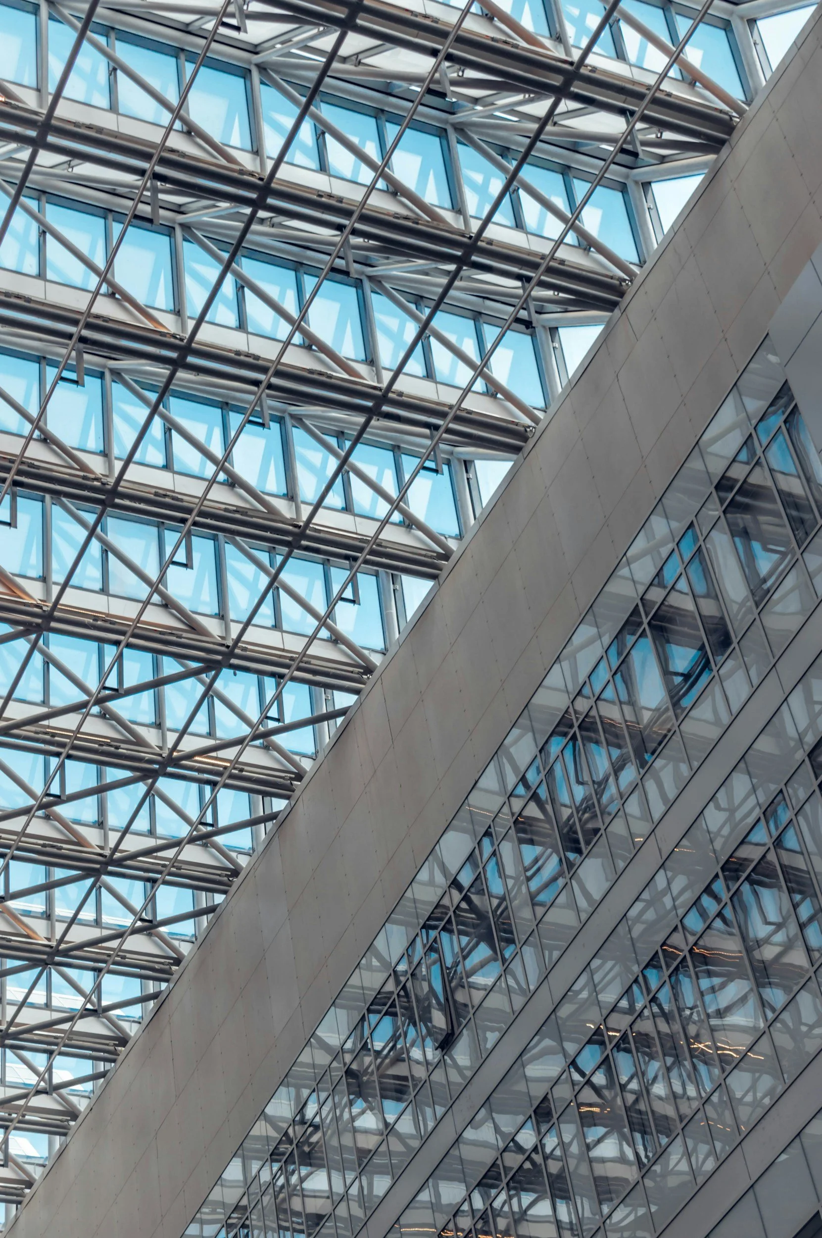 Close-up view of a modern building's interior featuring a glass window ceiling and a wall with reflective glass panels, showcasing architectural design with steel framework and geometric patterns.