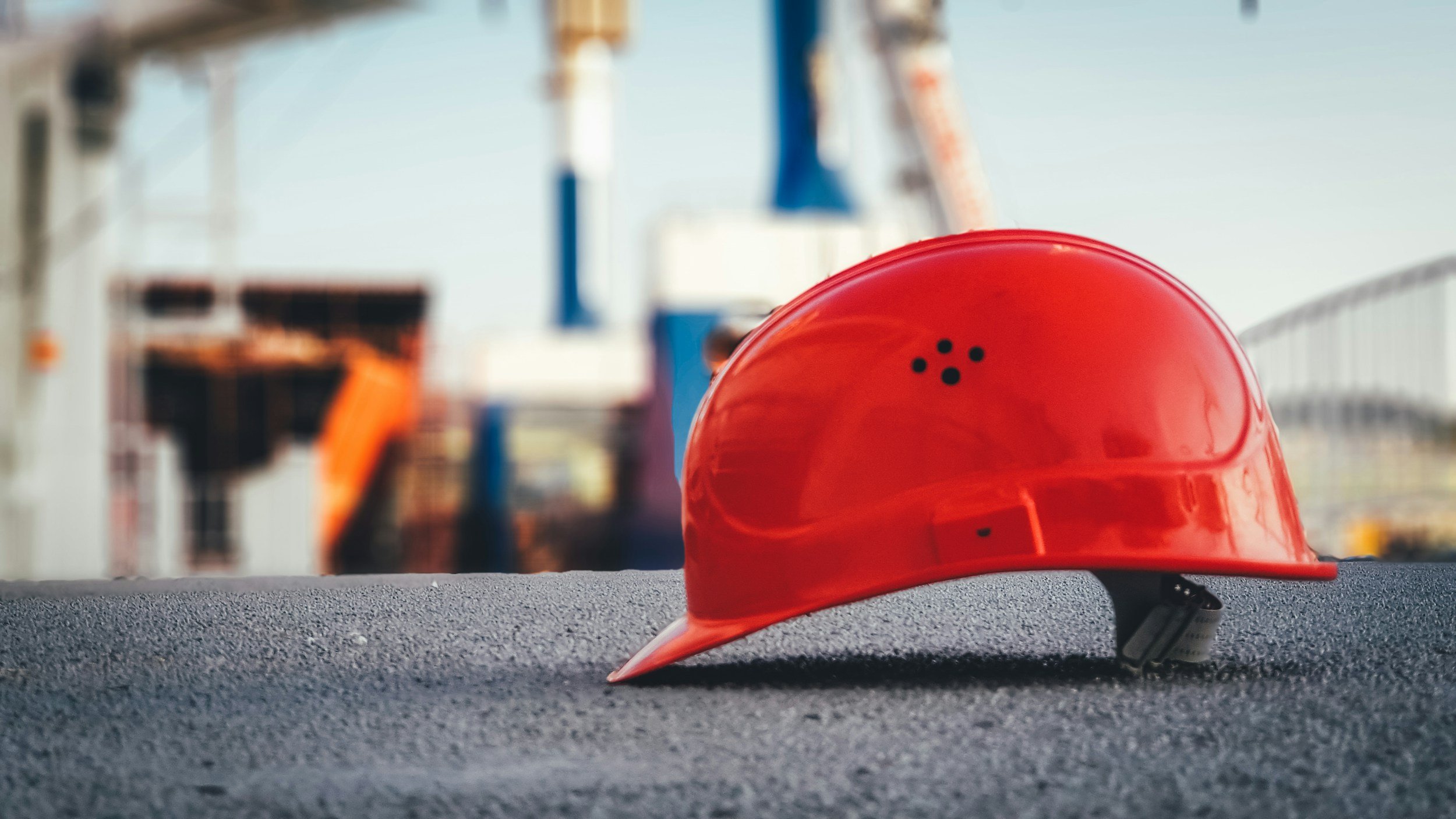 Red safety helmet resting on black textured surface with construction site in the background.
