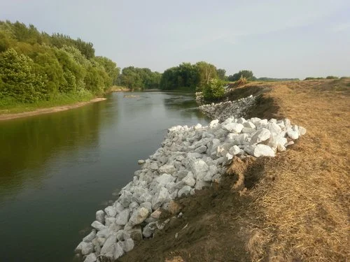 A river with a pile of rocks along the bank under a clear sky.
